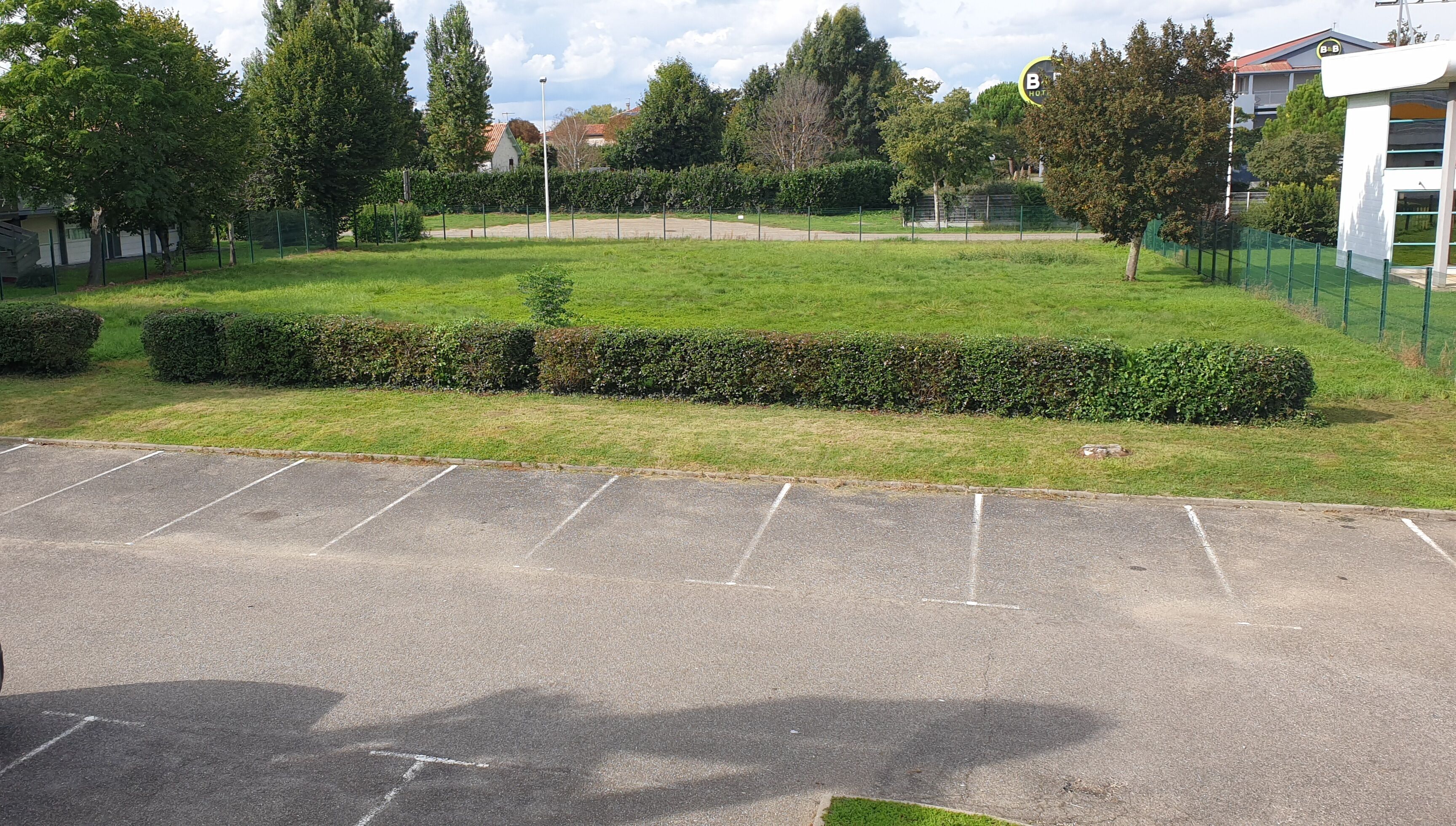 Ein Parkplatz mit einer grünen Hecke und einem Gebäude mit dem Schild "BB Hotel".