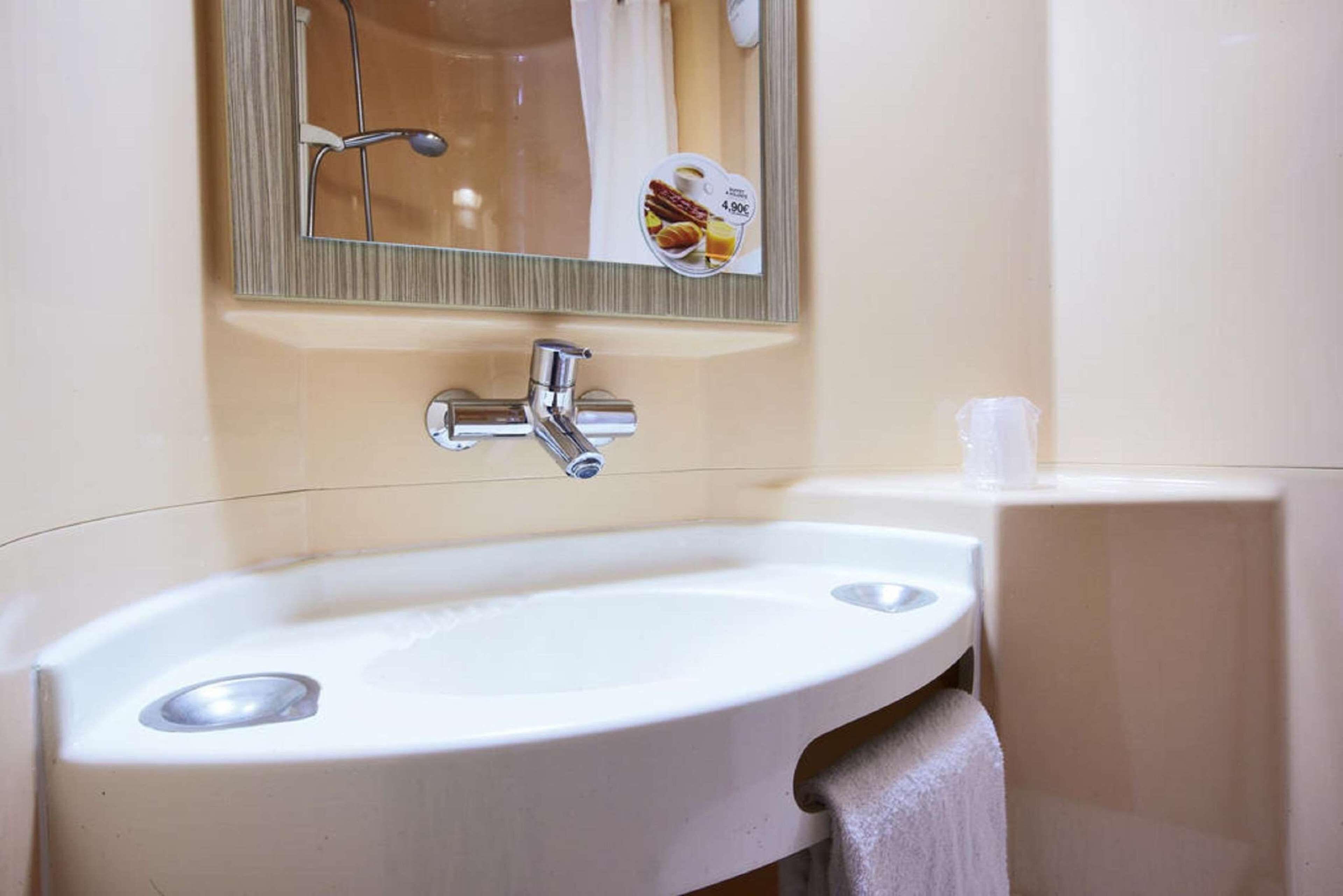 Un baño con lavamanos blanco, un espejo y un perchero para toallas.