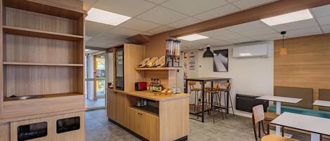 A modern cafe interior with wooden furniture, a counter with food items, and a seating area with tables and chairs.