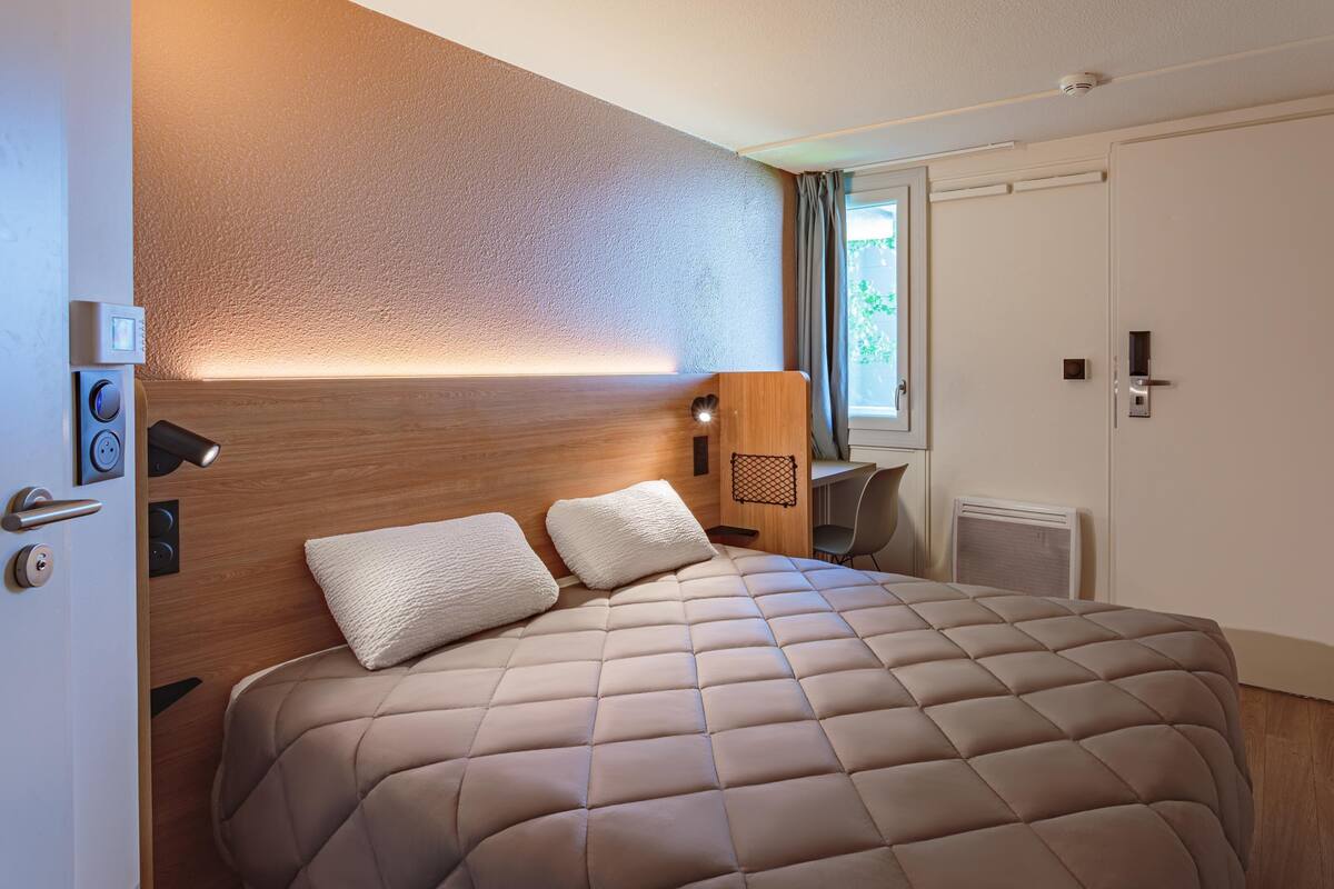 Quarto com cama, cabeceira de madeira, escrivaninha, cadeira e porta.
