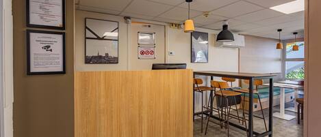 A reception area with a wooden desk, multiple chairs, a bulletin board with notices, a digital clock, and a window with a view of greenery.