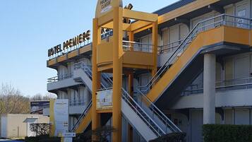 Un hotel de varios pisos con una fachada amarilla destacada, una escalera central y un letrero que indica que es un hotel de primera clase.