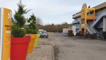 A hotel entrance with a sign for "Hotel Premier Classe" and a parking area with a car.