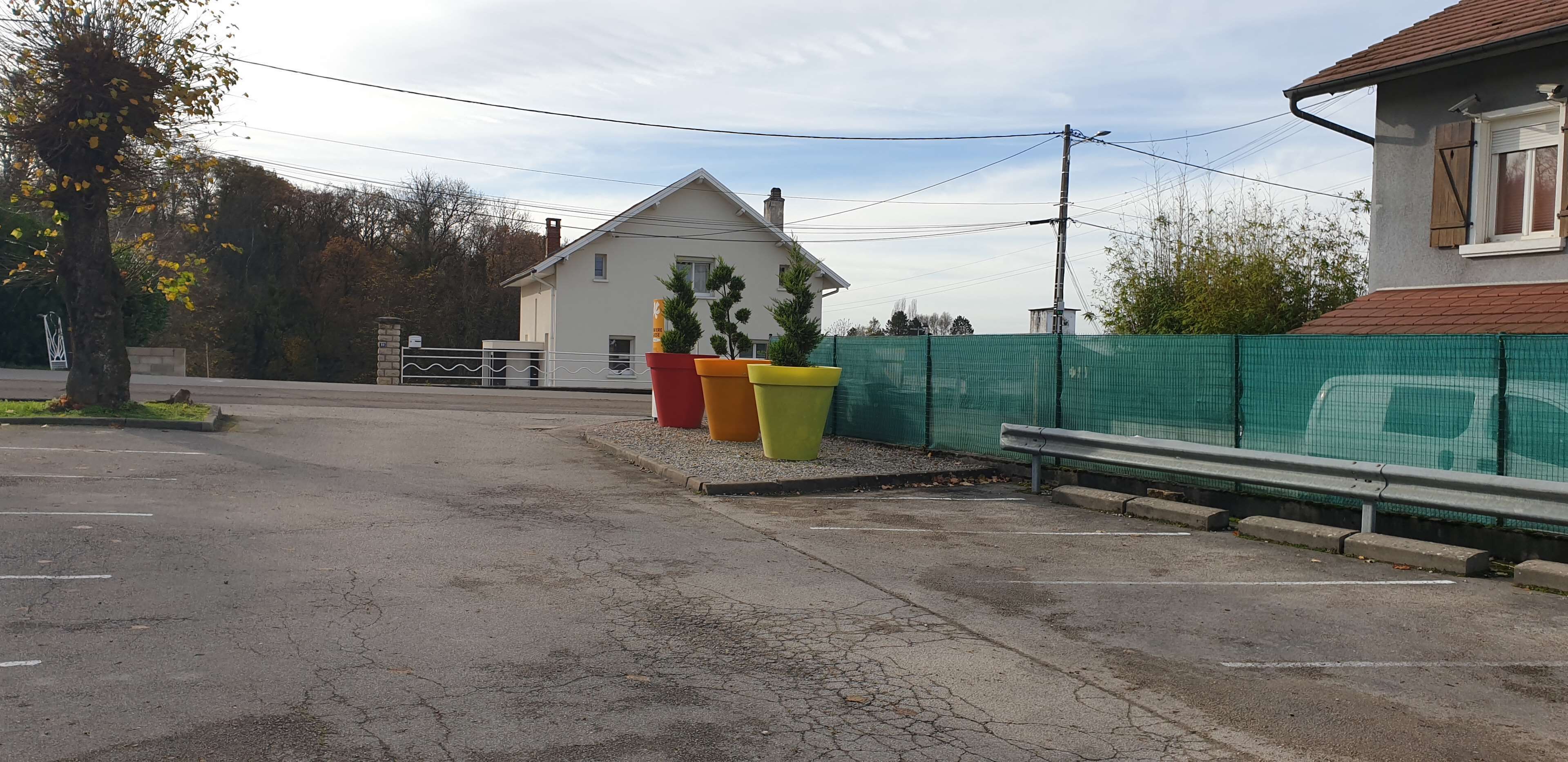 Una calle residencial con una casa, una valla verde y macetas coloridas.
