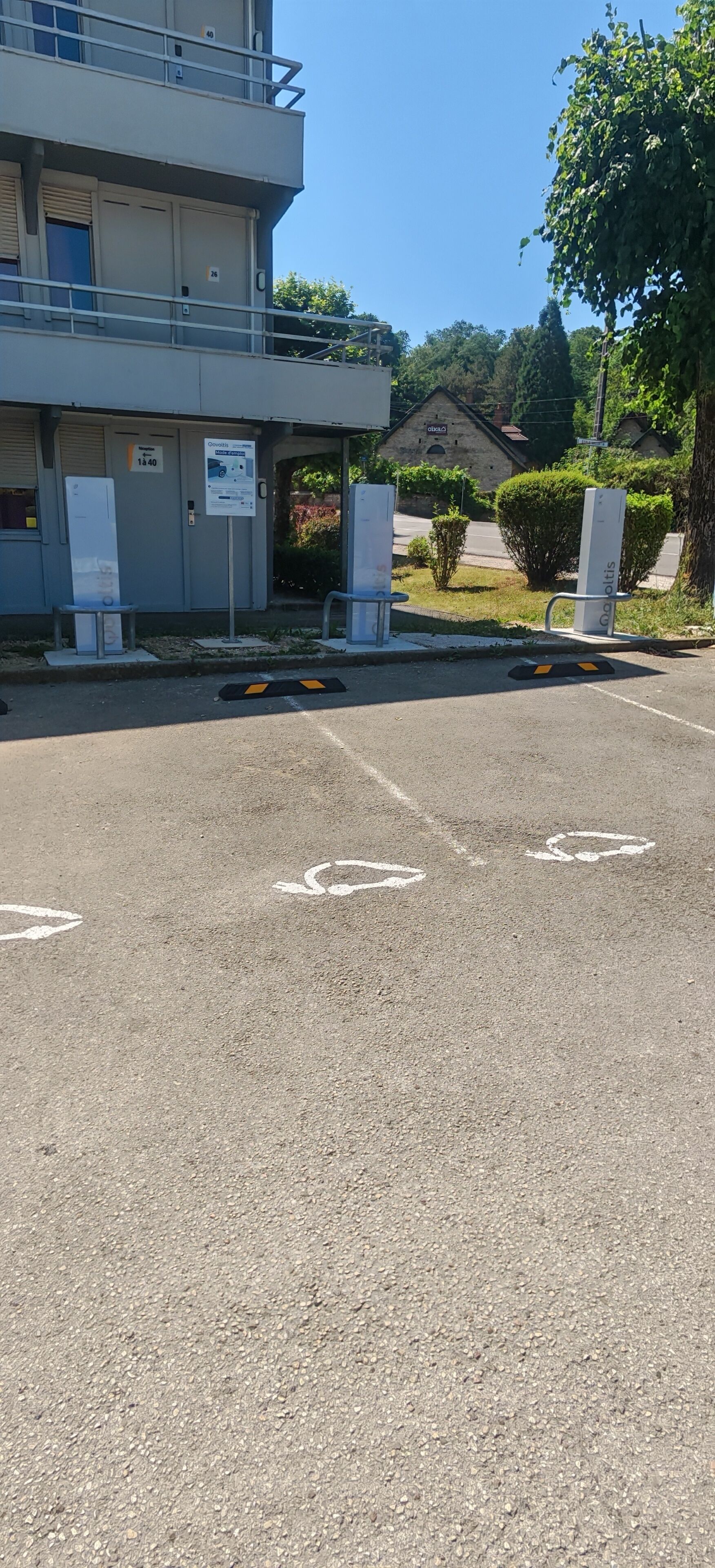 A parking area with marked spaces, a building with a sign, and a small structure in the background.