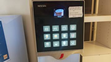 A Nescafé coffee machine with a touchscreen interface, a coffee cup icon, and a red button below.