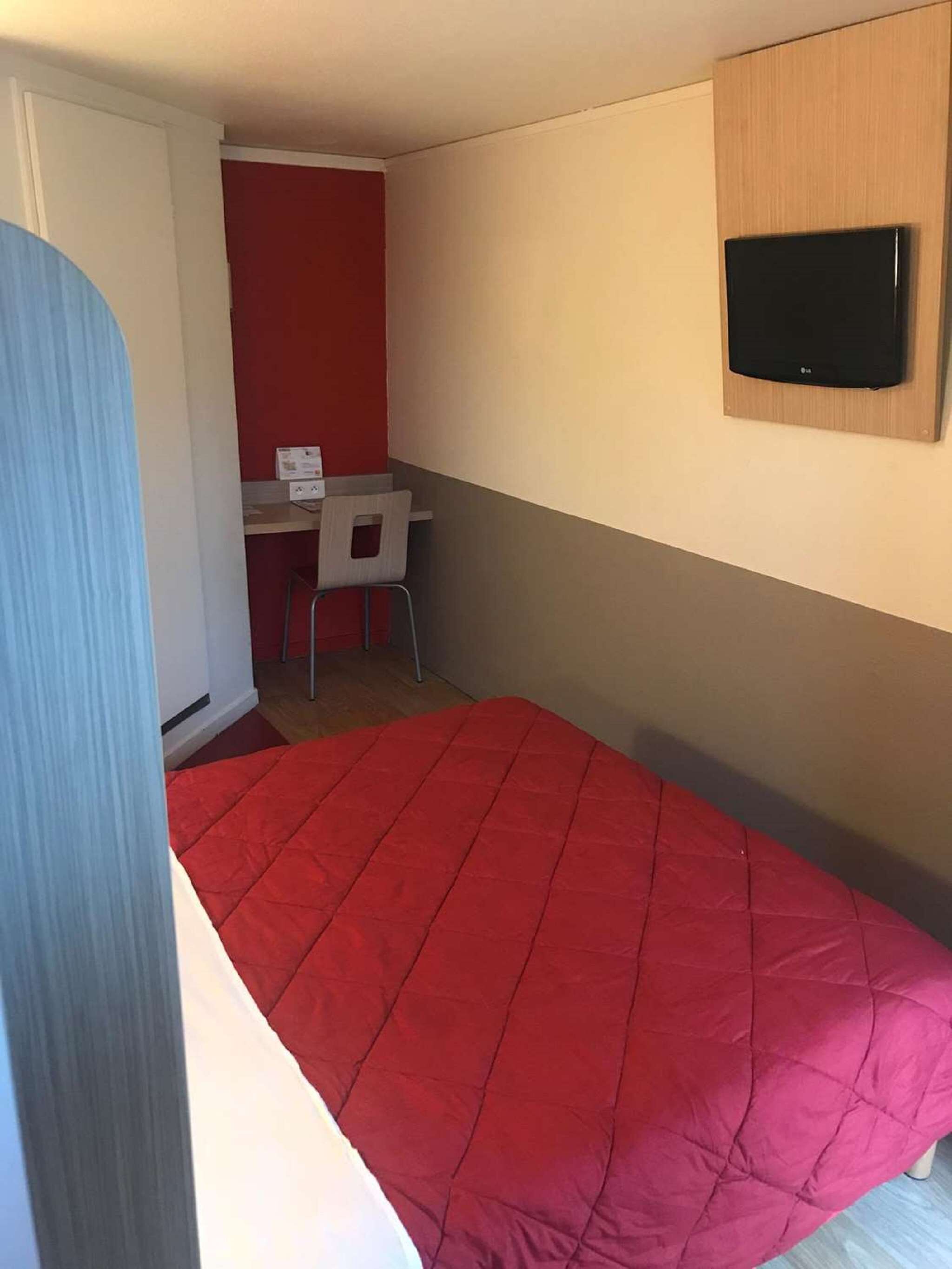 Une petite pièce, de taille modeste, comprenant un lit simple, un bureau et un téléviseur.