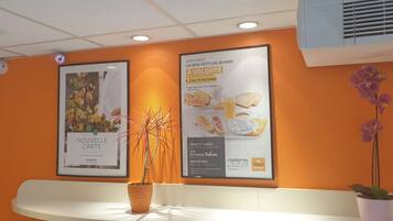 Une salle d’attente aux murs orange, avec un comptoir d’accueil blanc et deux plantes en pot.