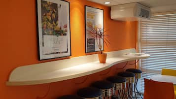 A modern bar area with a curved white shelf displaying framed posters, a potted plant, and a bar stool.
