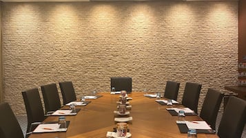 A conference room with a long wooden table, black chairs, and a stone wall.