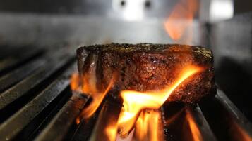 Bife grelhado na churrasqueira, com chamas visíveis.
