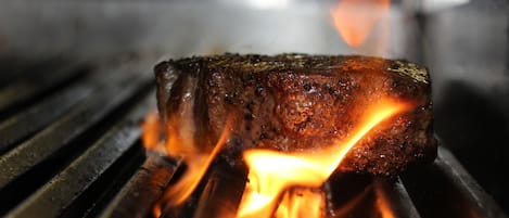 A steak grilling on a grill with visible flames.
