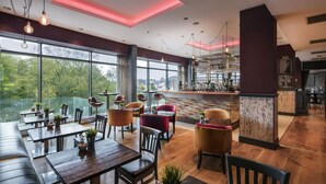 A modern restaurant with wooden tables and chairs, large windows, and a bar area. - Absolute Hotel Limerick (Limerick)