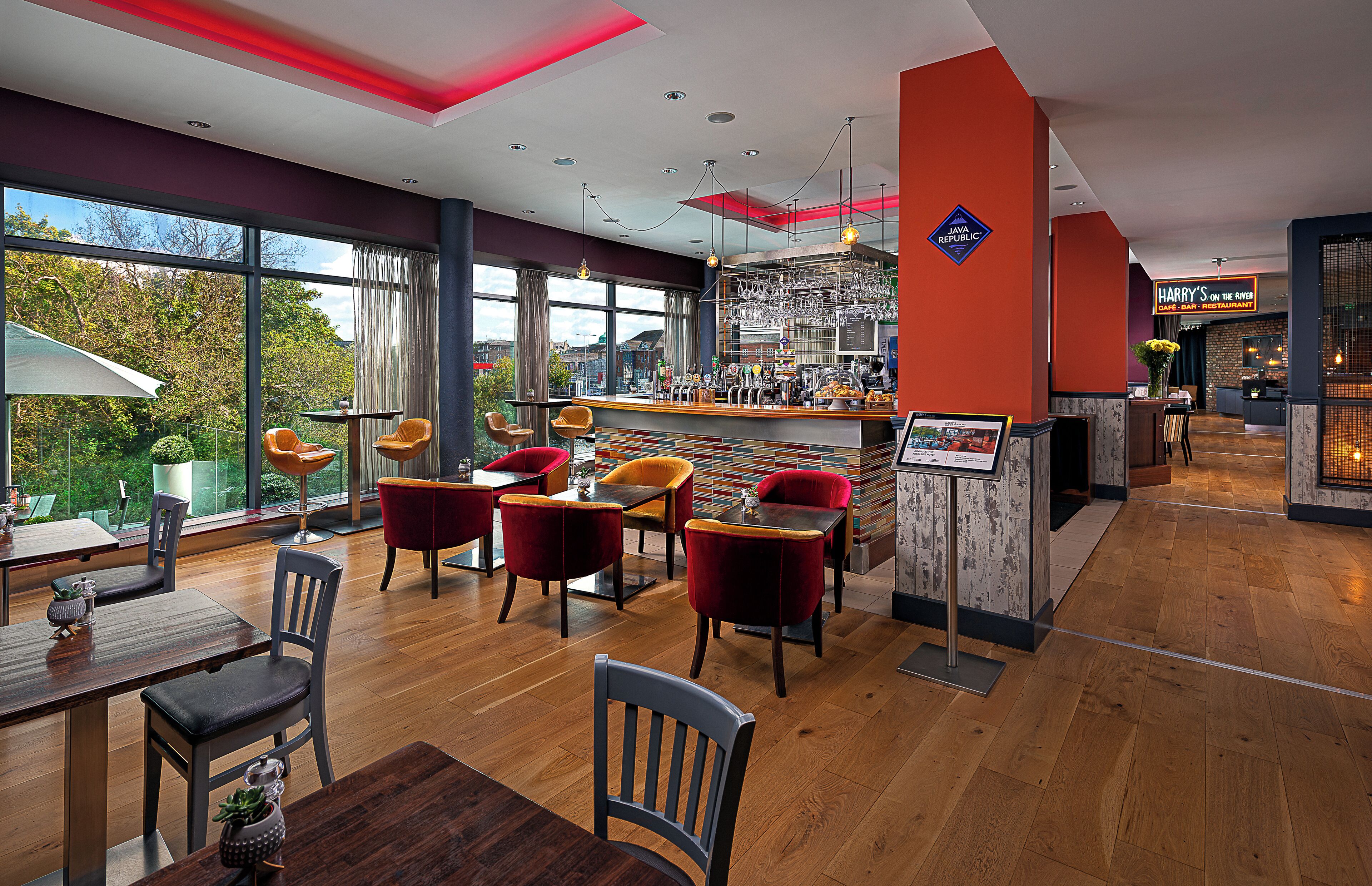 Un restaurante moderno con zona de bar, suelo de madera y sillas rojas y grises.