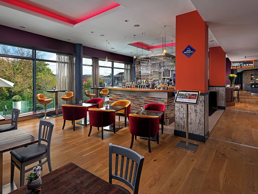 Un restaurante moderno con zona de bar, suelo de madera y sillas rojas y grises.
