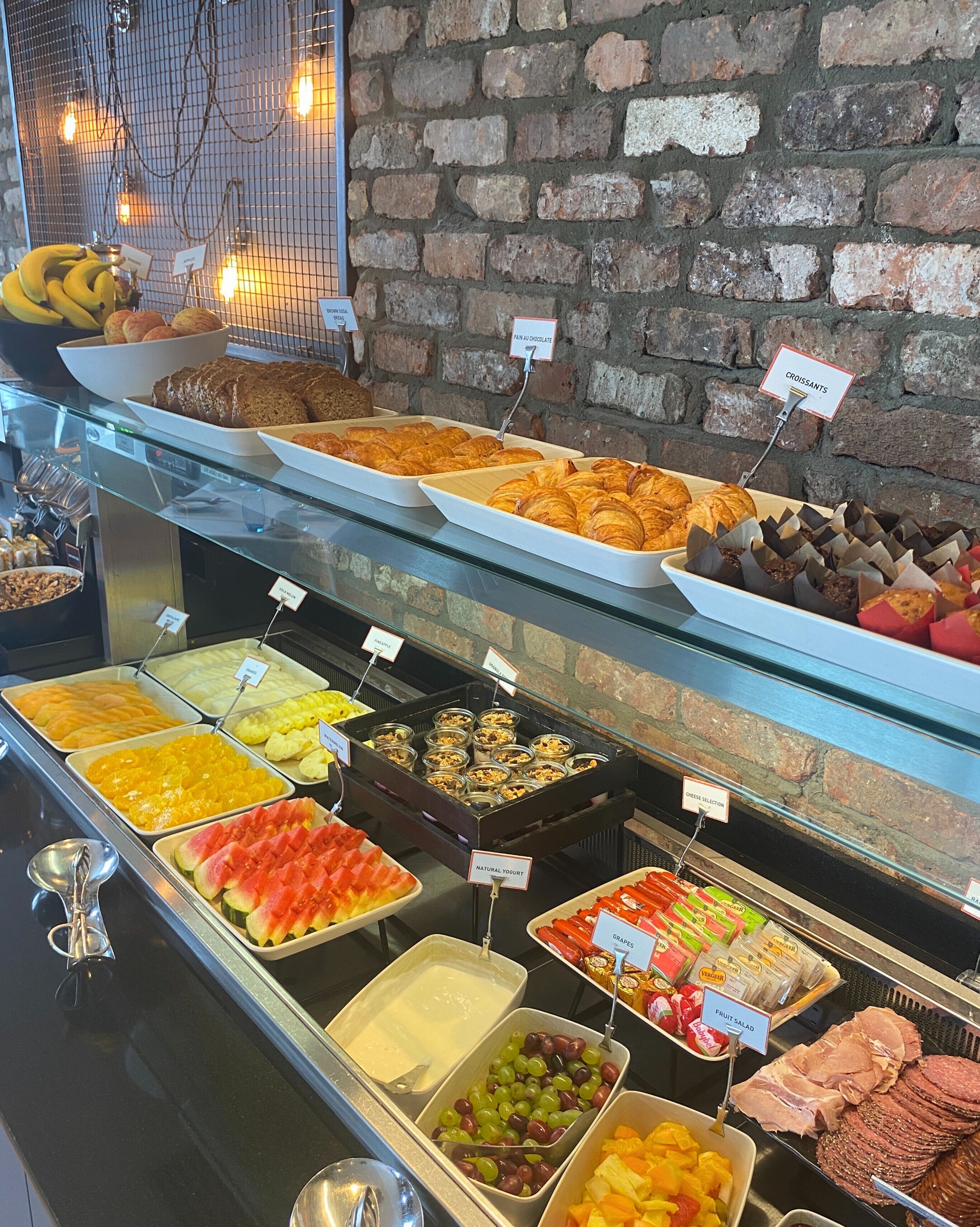 A buffet with various food items including fruits, pastries, and meats.