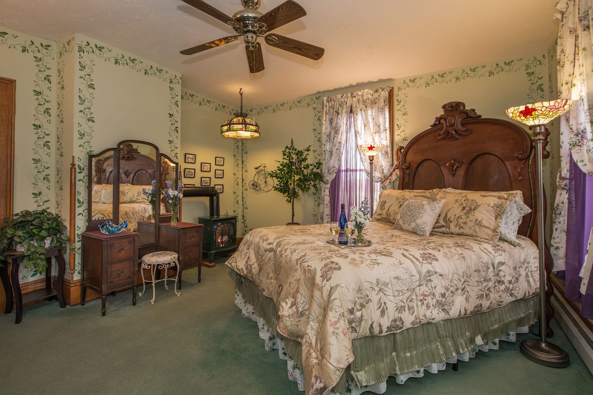 A bedroom with a large bed, a ceiling fan, a dresser, a mirror, a lamp, and a potted plant.