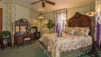A bedroom with a large bed, a ceiling fan, a dresser, a mirror, a lamp, and a potted plant.