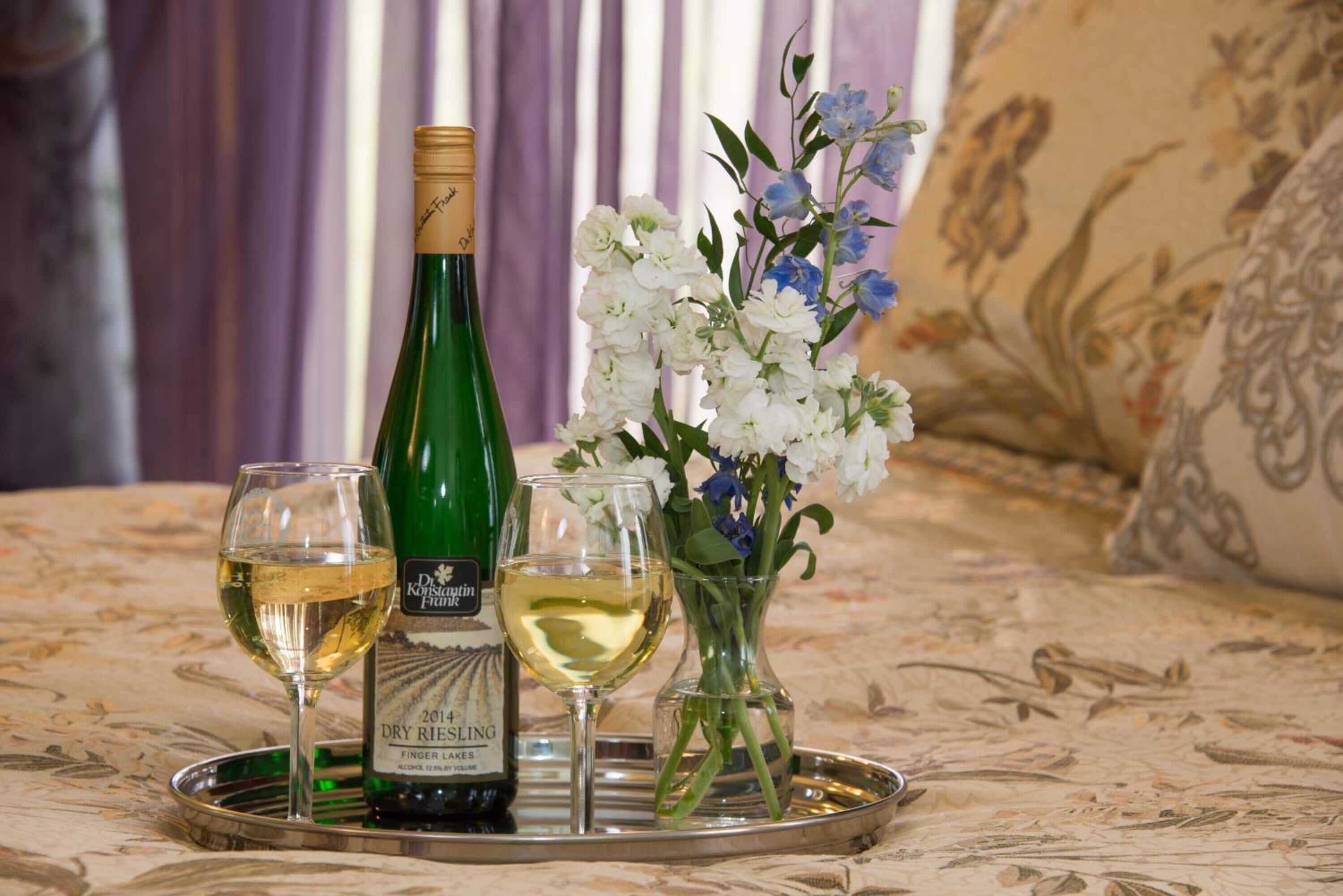 Eine Flasche trockener Riesling aus dem Jahr 2014, zwei Weingläser und eine Vase mit Blumen auf einem Tablett.