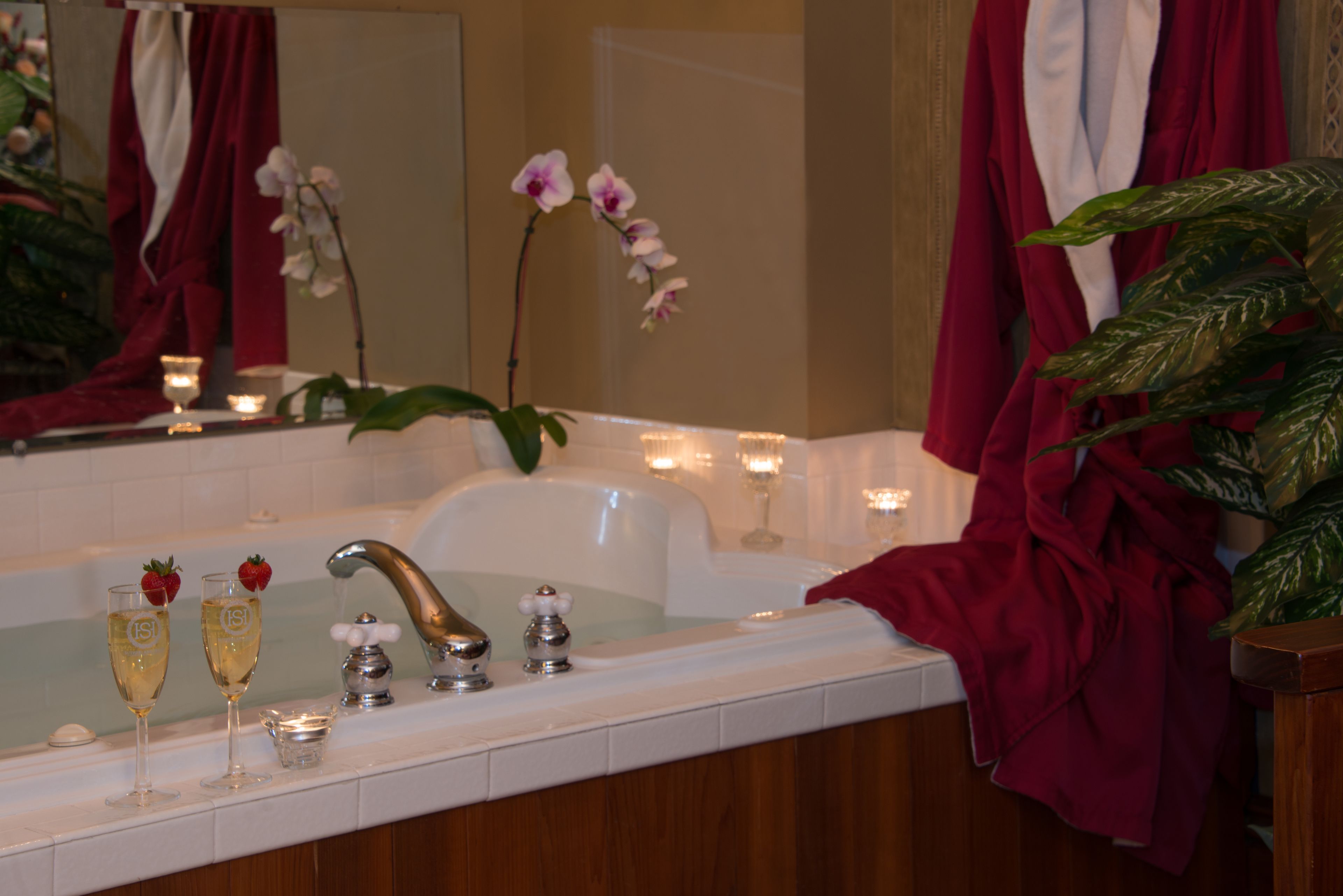 A bathroom with a bathtub, a sink, and two champagne glasses with strawberries. There are candles and a potted plant.