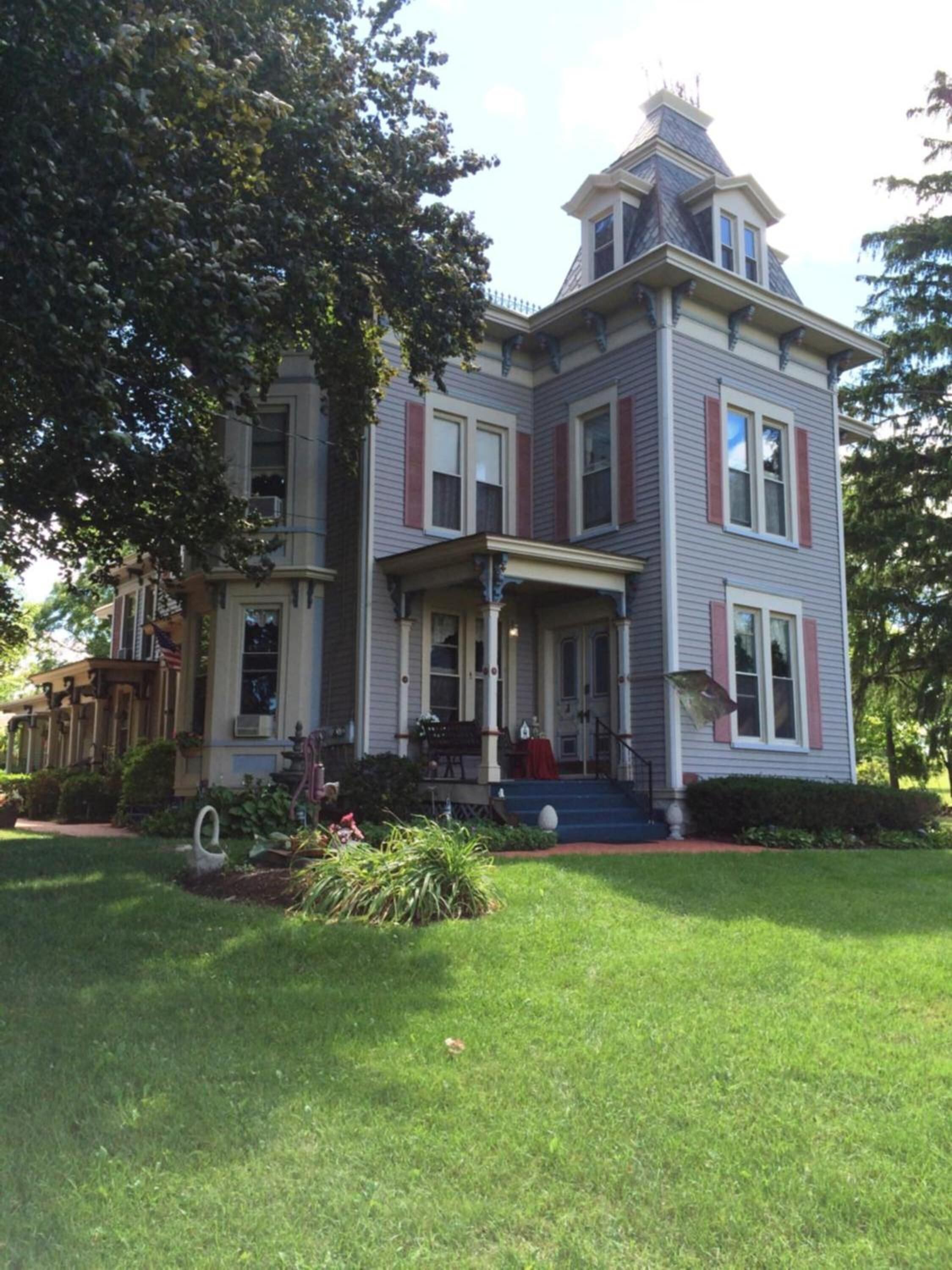 A two-story house with a wrap-around porch, a small front yard, and a large tree to the left.