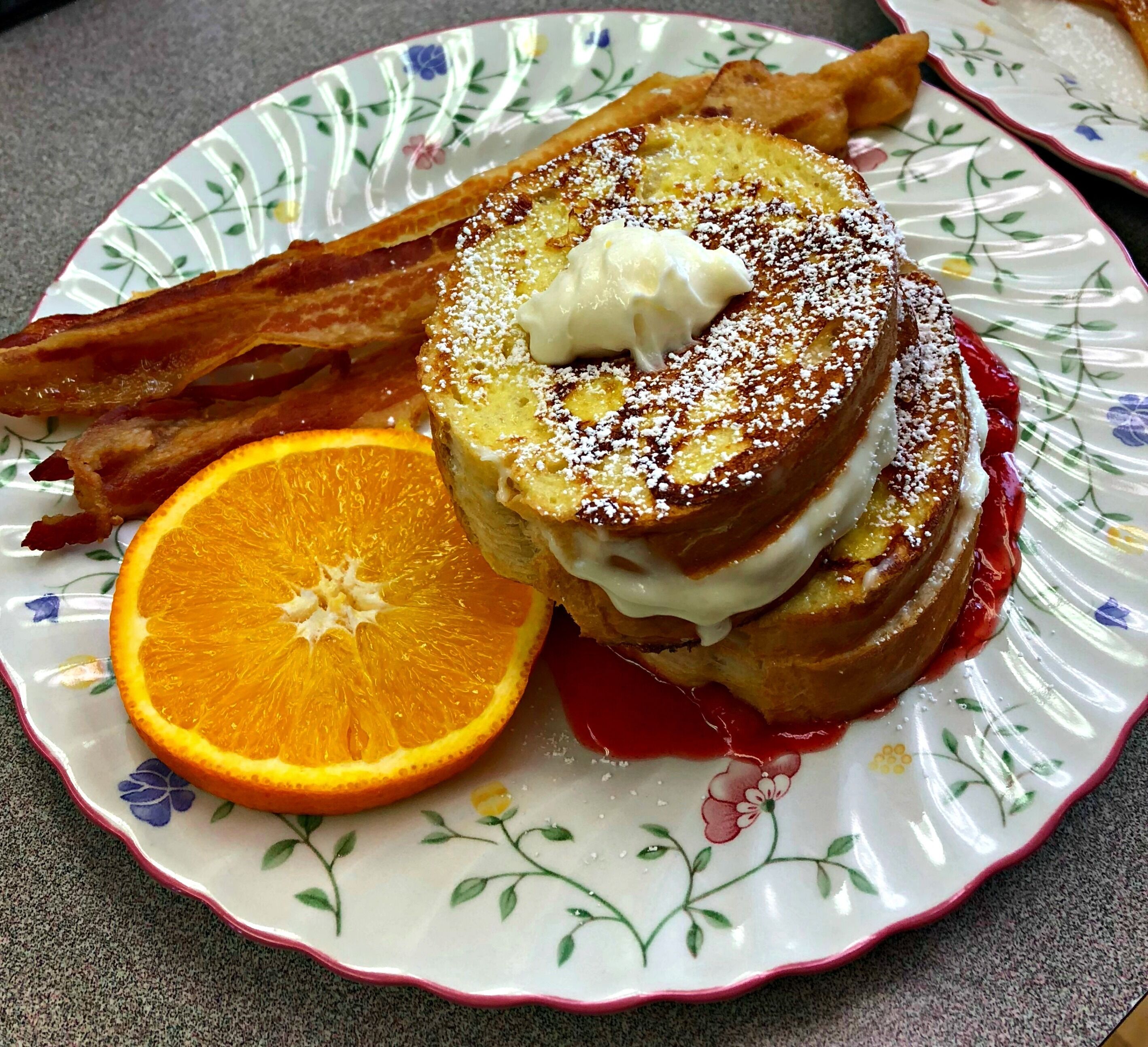 Une assiette avec des tranches de pain perdu, du bacon et une tranche d’orange.