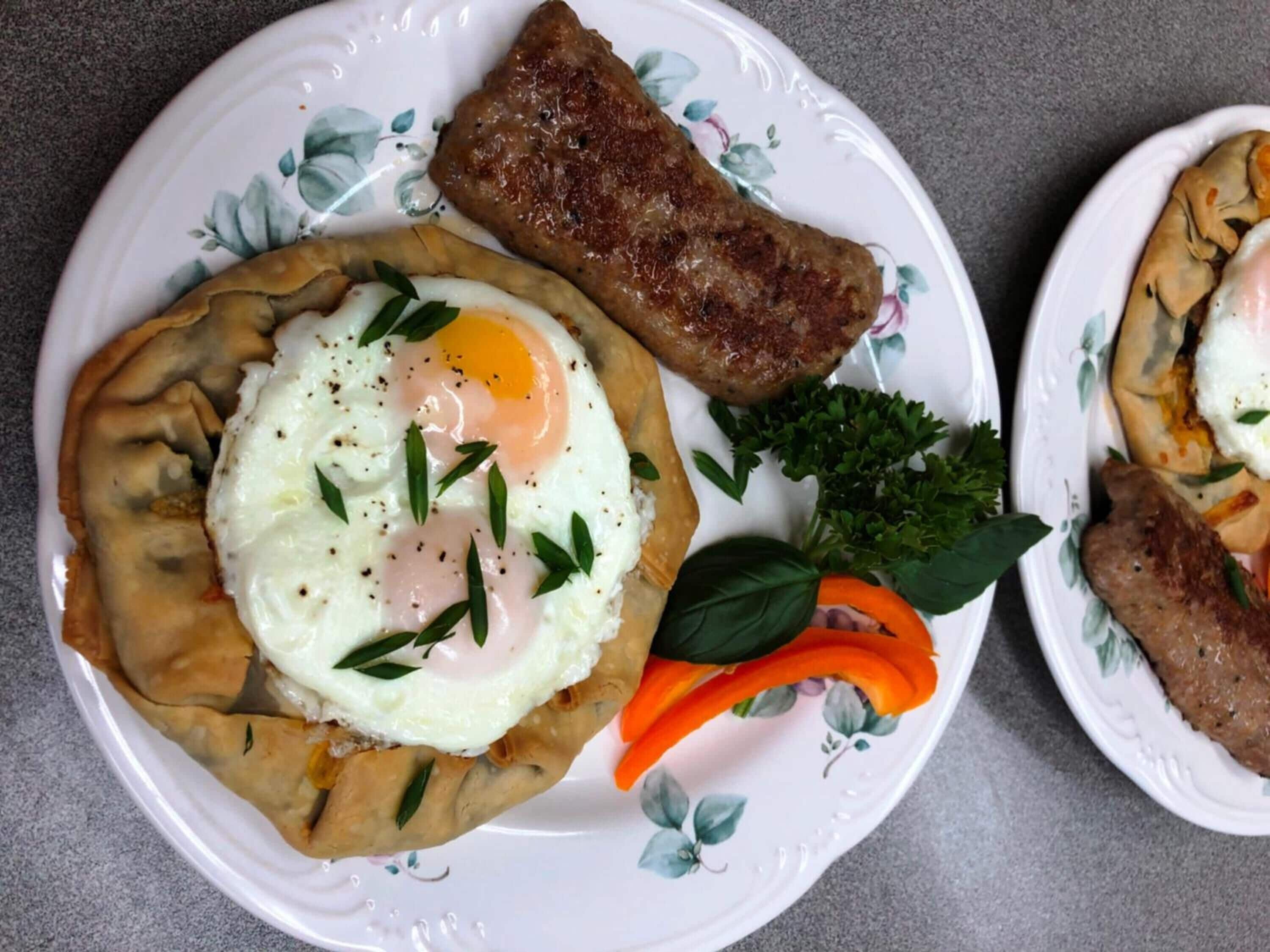 A plate with a stuffed pastry topped with a fried egg, a piece of grilled meat, and some vegetables.