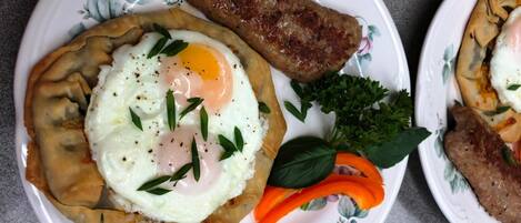 A plate with a stuffed pastry topped with a fried egg, a piece of grilled meat, and some vegetables.