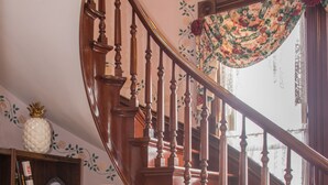 En trætrap med et blomstret gardin, en træstol, et bord med en lampe og en reol med forskellige genstande.