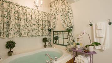 A bathroom with a freestanding bathtub, floral curtains, a vanity with a mirror, and towels hanging on hooks.