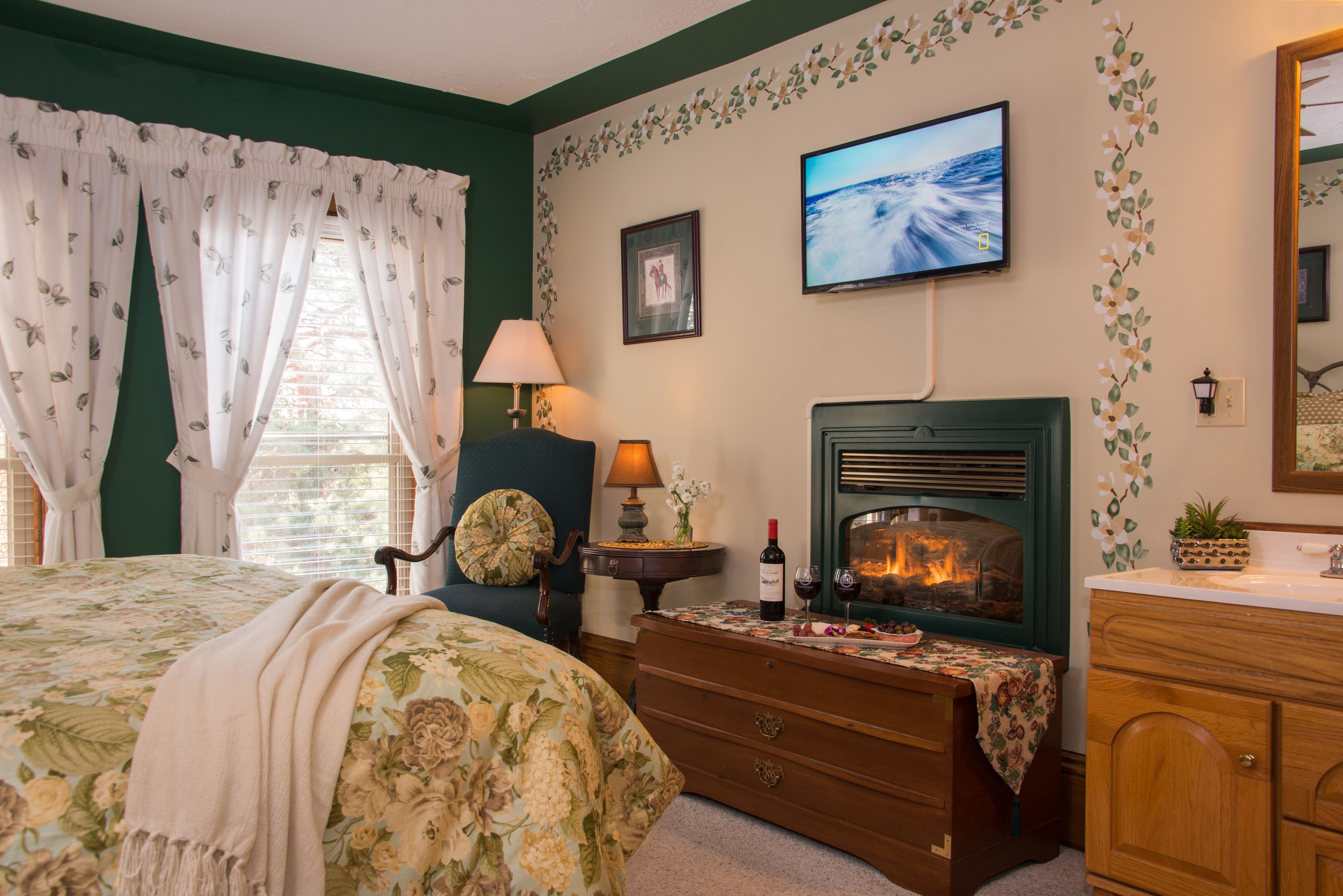 Un dormitorio con cama, cómoda, chimenea, televisor y ventana con cortinas.