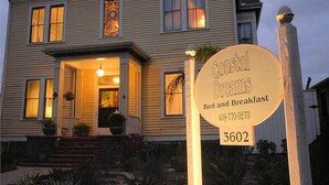 A two-story house with a sign for Coastal Dreams Bed and Breakfast, featuring a welcoming entrance with steps and potted plants.