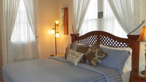 A bedroom with a wooden bed, white curtains, a bedside lamp, and a nightstand.