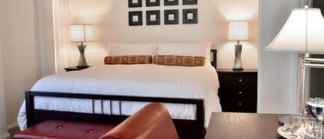 A hotel room with a bed, two bedside tables with lamps, a red chair, and a small table with glasses.