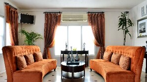 A living room with two orange sofas, a round coffee table, and a large window with curtains. - El Primero Hotel (Chula Vista)