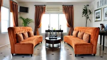 A living room with two sofas, a round coffee table, a TV mounted on the wall, and a large window with curtains.