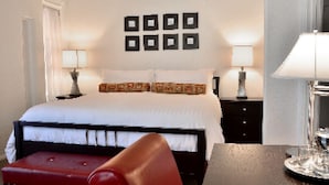 A hotel room with a large bed, two bedside tables with lamps, a red chair, and a wall with six square mirrors. - El Primero Hotel (Chula Vista)