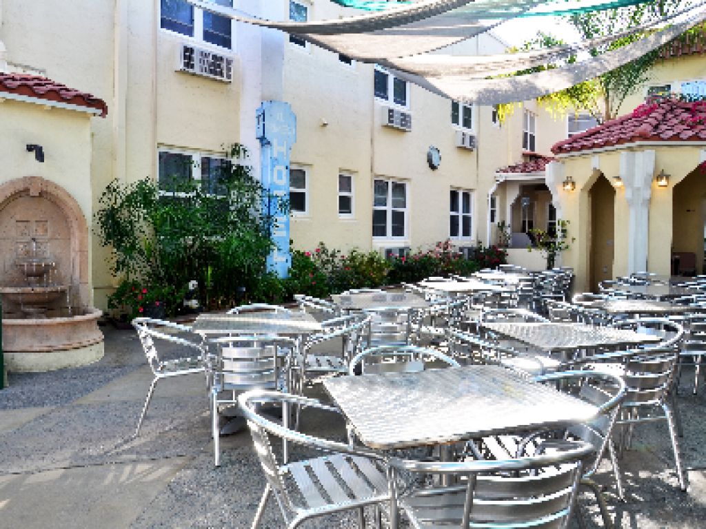 Una zona patio all'aperto con diversi tavoli e sedie, una fontana e un edificio con balconi.