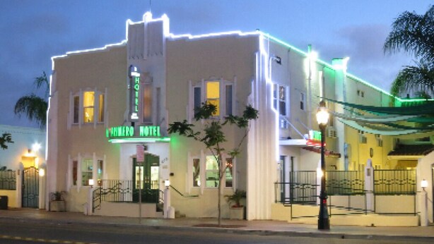 Un hôtel à la façade classique, avec un drapeau au sommet et un panneau lumineux au néon.