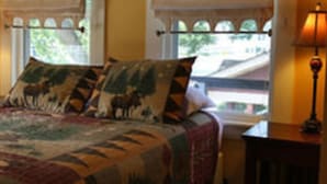 A bed with a patterned bedspread, two bedside lamps, and a window with a view of the outside. - Wildcat Inn & Tavern (Jackson)