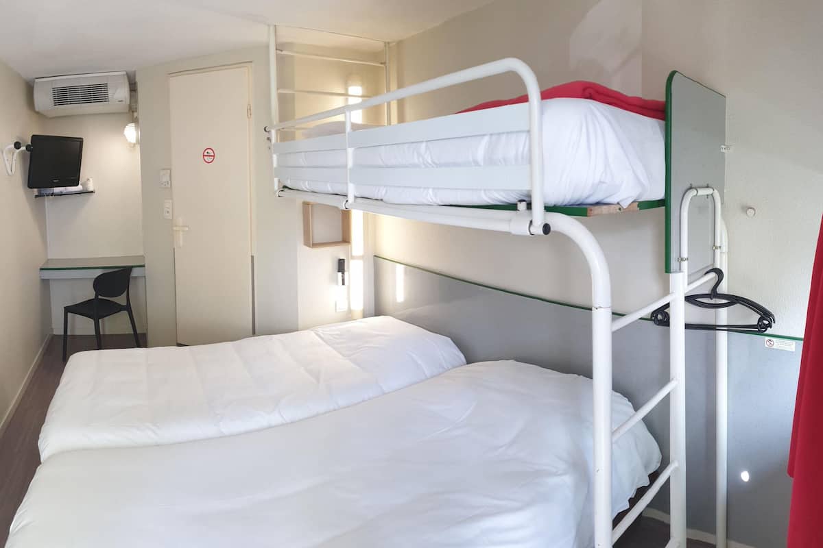 Quarto com beliche, escrivaninha e cadeira, um computador e uma porta com placa de proibido fumar.