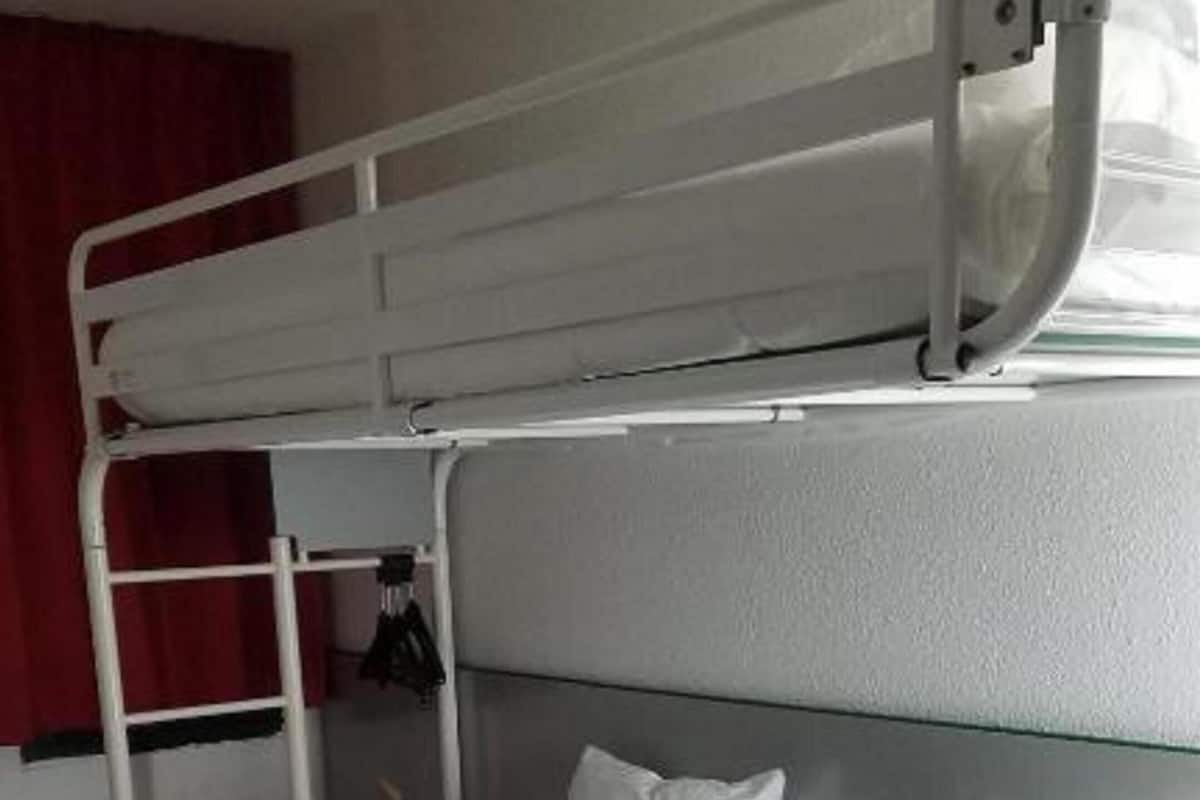 Uma cama beliche com duas almofadas, uma escada e uma janela com cortinas.