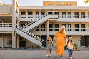 Il s'agit d'un hôtel dont l'enseigne indique « HÔTEL PREMIÈRE CLASSE ». Il se distingue par son architecture à plusieurs niveaux, avec un escalier, un espace extérieur aménagé pour s'asseoir et un petit jardin.