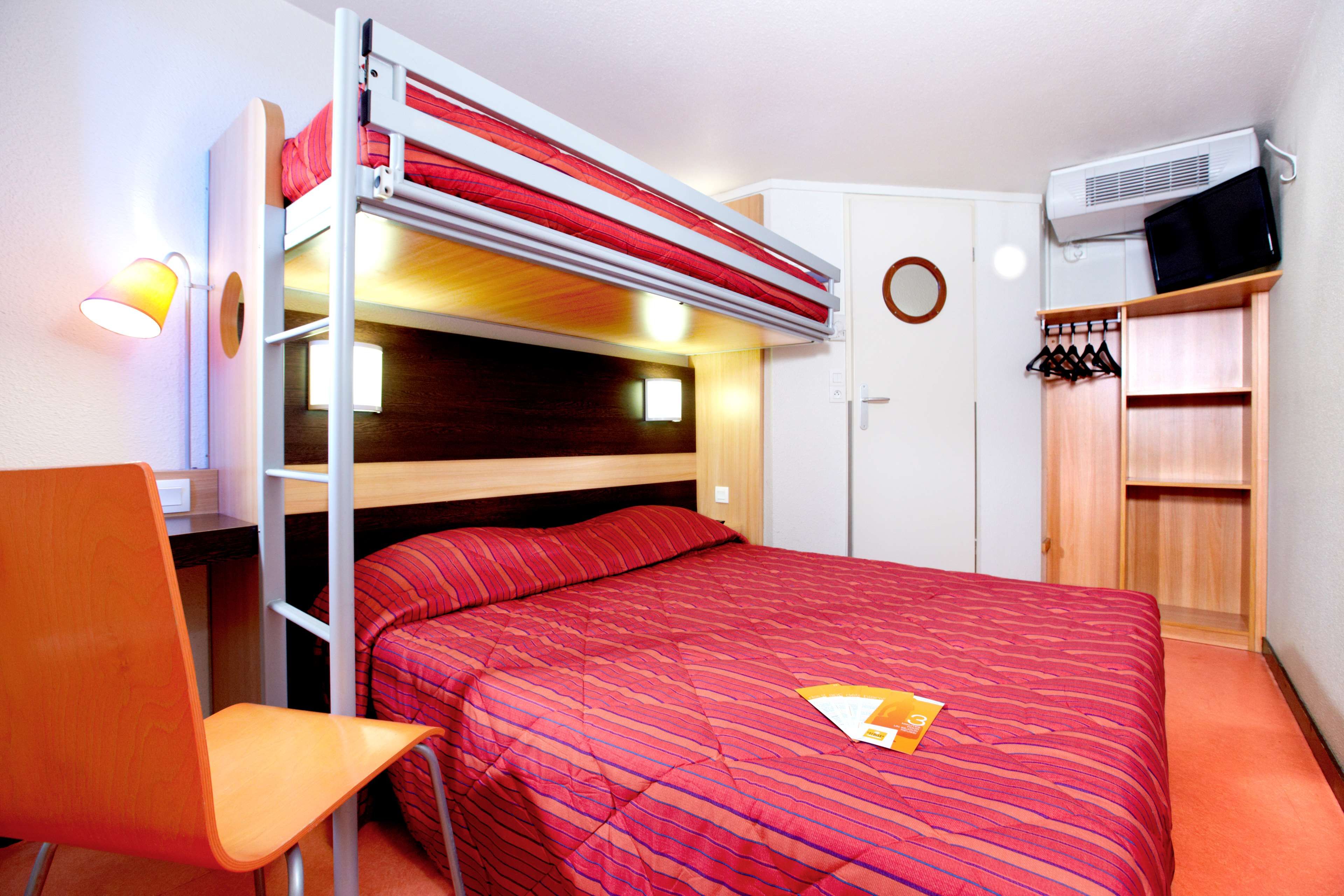 A bunk bed with a red striped mattress, a single bed with a red blanket, a wooden chair, a wardrobe, and an air conditioning unit.