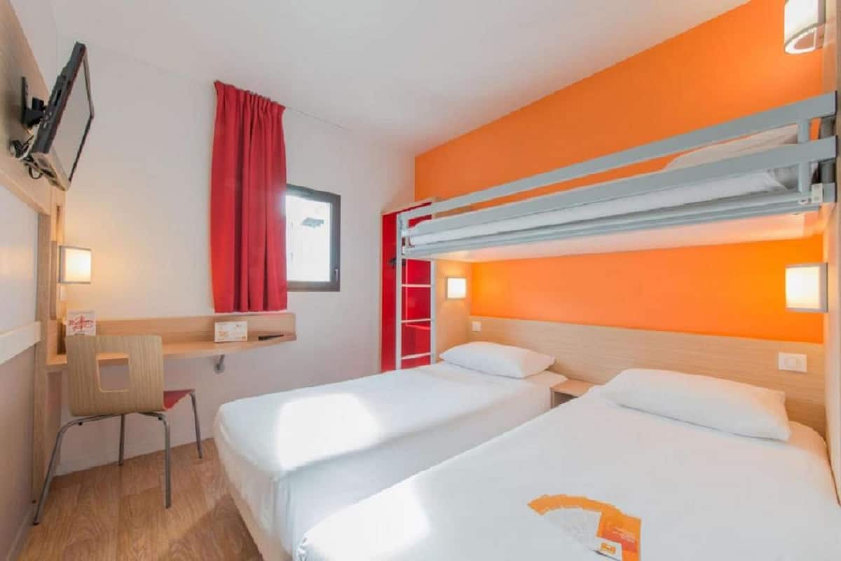 Une chambre d’hôtel avec deux lits, un bureau, une chaise et un lit superposé.