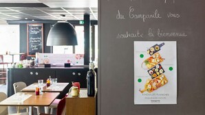 A restaurant interior with tables, chairs, a chalkboard menu, and a poster on the wall.