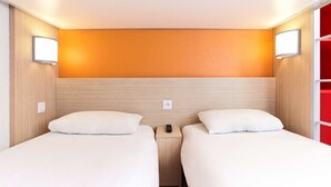 A hotel room with two beds, wooden headboards, and a red accent wall.