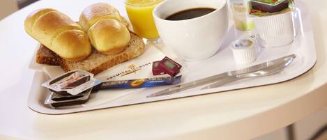 A breakfast tray with bread rolls, a glass of orange juice, a cup of coffee, and various condiments.