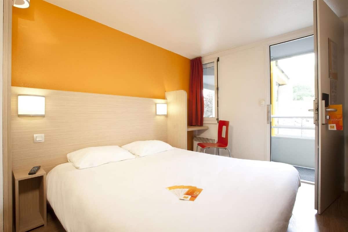 Une chambre d’hôtel comprenant un lit, un bureau, une chaise et une porte coulissante donnant sur le balcon.