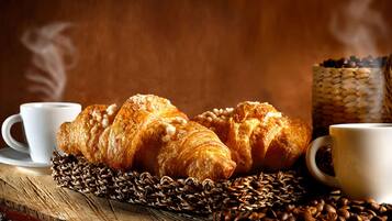 Cornetti, tazze di caffè e chicchi di caffè su un ripiano di legno.